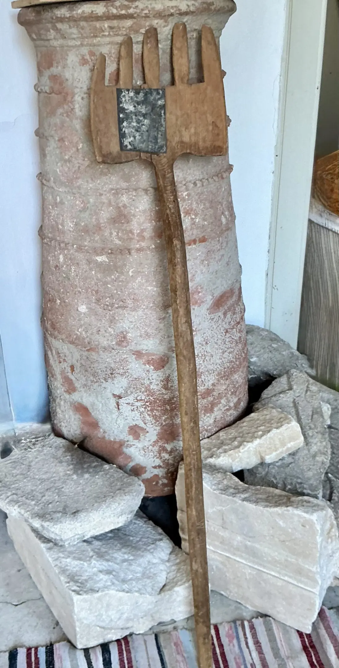 Antique wooden rake leaning against clay urn